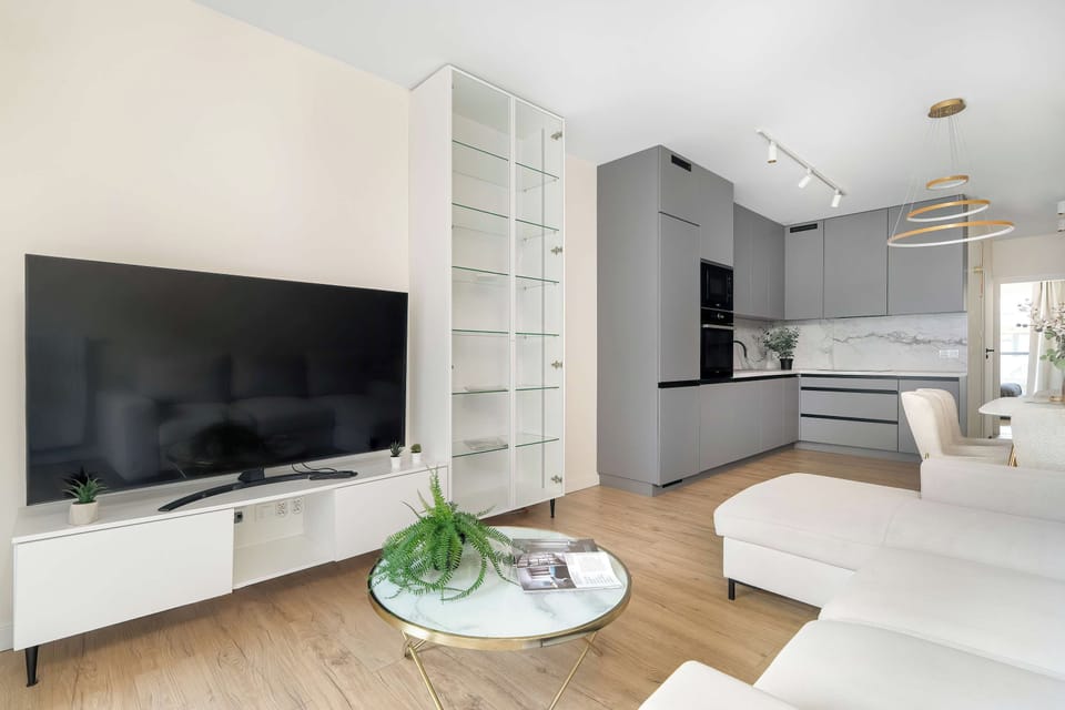 A straight-on view of the living room's entertainment setup shows a large flat-screen TV resting on a long white media console. Tall white open shelving stands to the left of the television.