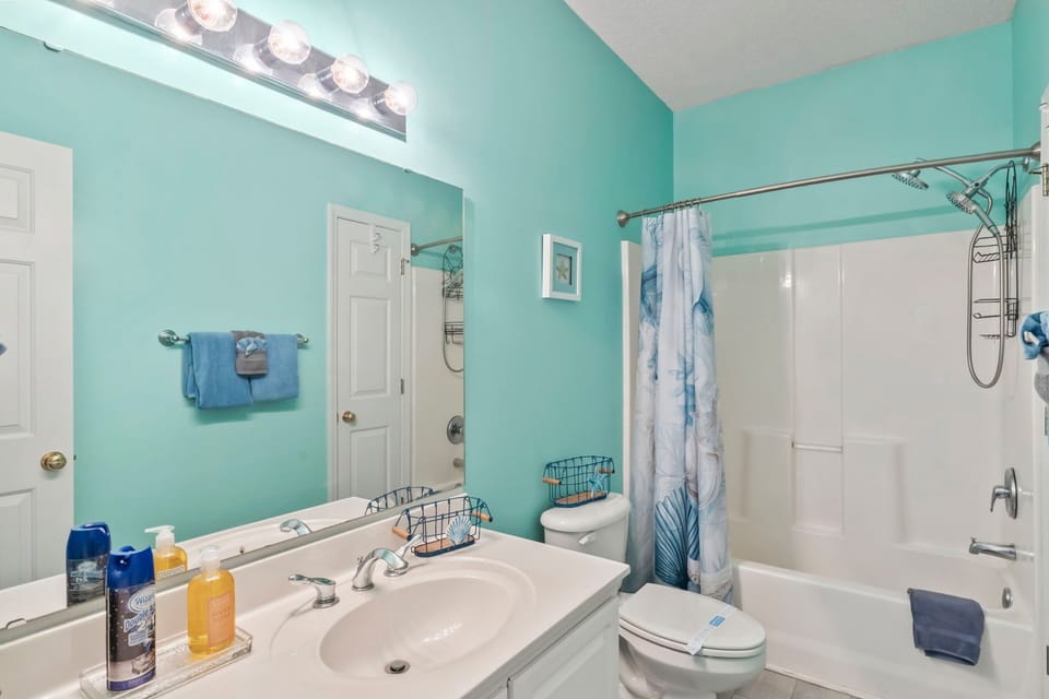 Full bathroom with bright turquoise walls, white vanity, and shower-tub combination.