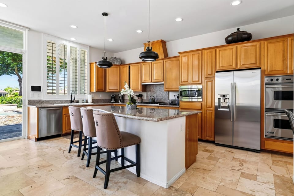 Contemporary kitchen with central island, pendant lighting, stainless appliances, and ample cabinetry.
