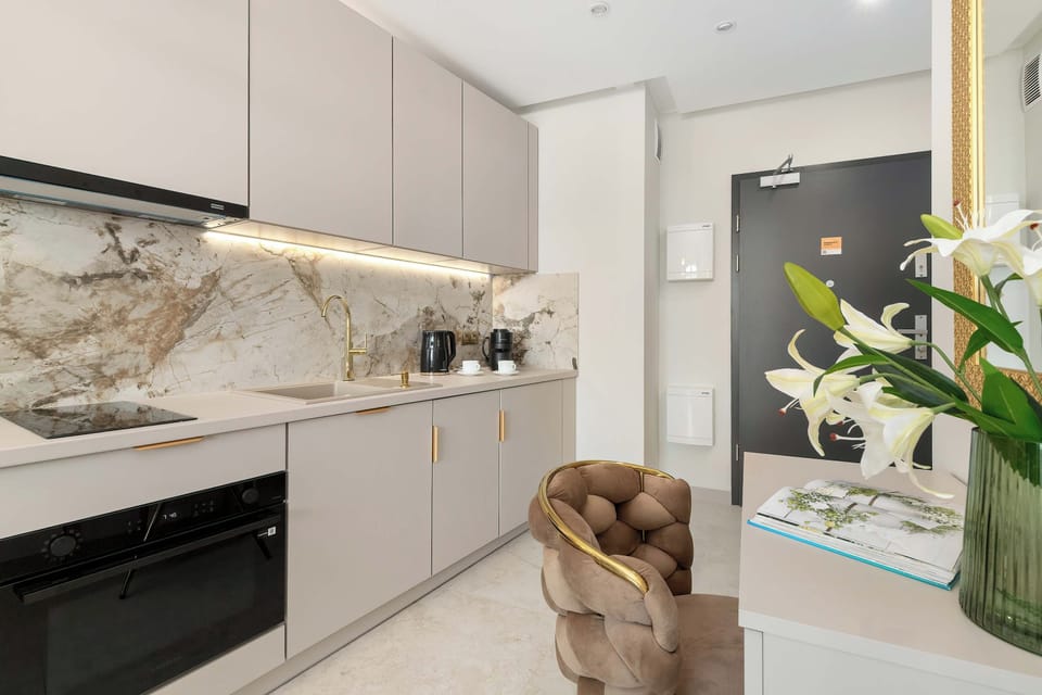 A bright kitchenette with white cabinets, marble backsplash, and a dining area.