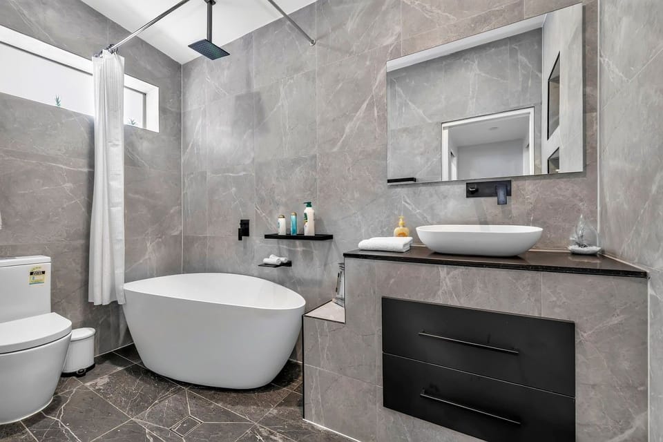 Freestanding tub with rain shower and marble-look tiling.