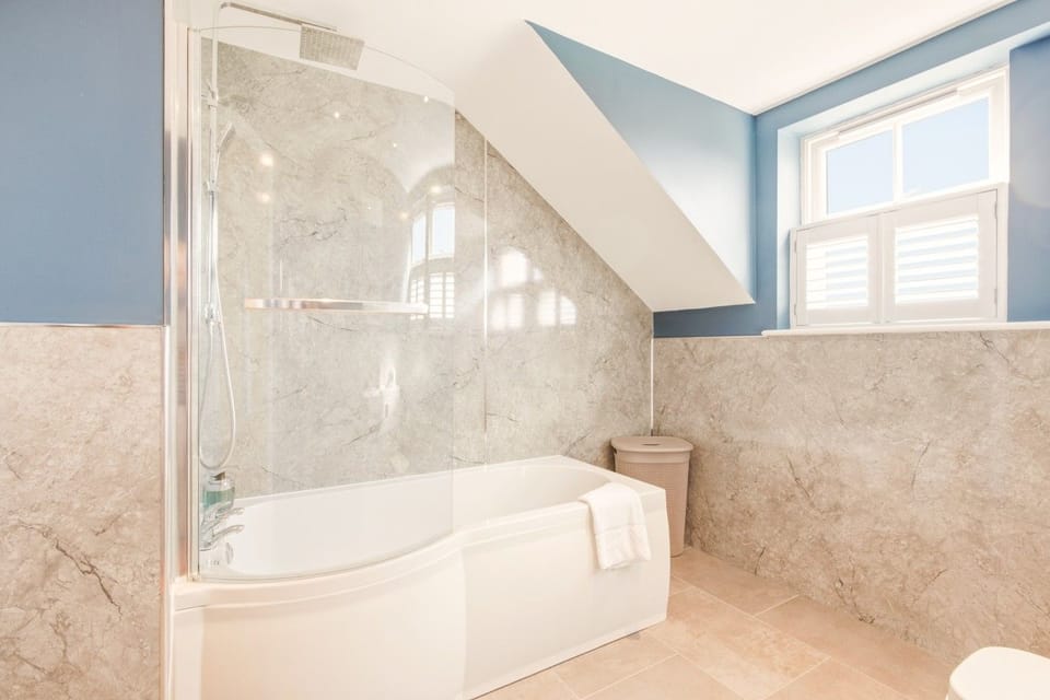 Bath with glass shower screen and natural light from shuttered window