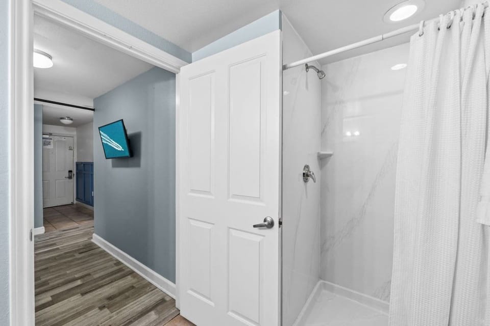 Step into the bright shower area featuring a clean white surround, curtain, and easy access from the adjoining hallway.