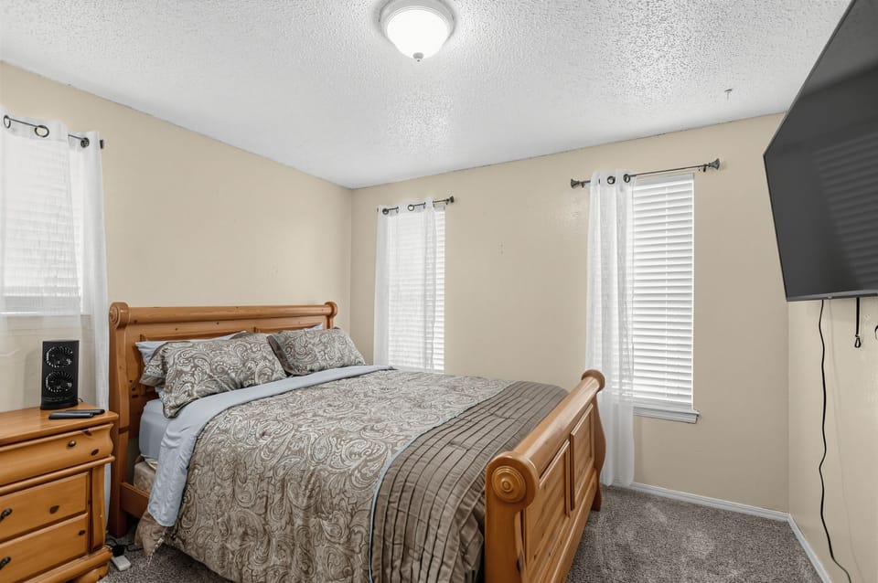 A cozy carpeted bedroom featuring a wooden bed, nightstand, and wall-mounted TV.