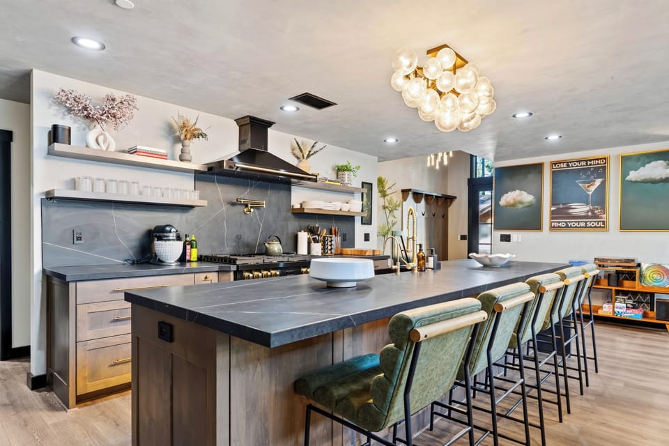 The polished kitchen features a spacious island with bar seating, wood cabinetry, open shelving, and sculptural lighting.
