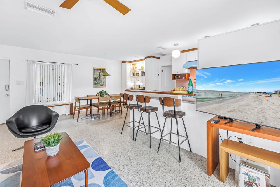 Bright open living space with breakfast bar, dining area, and large TV