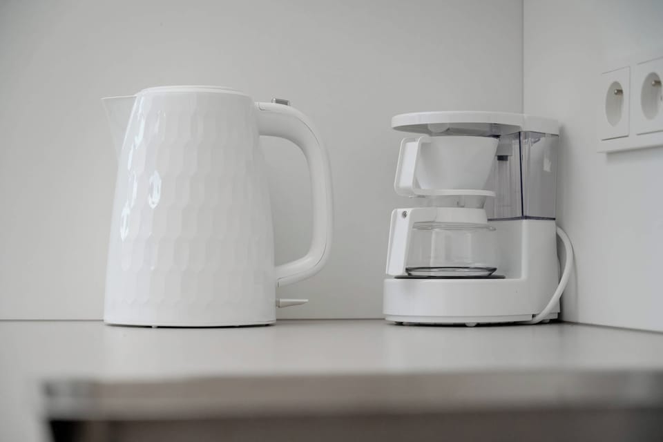 A close-up view of the kitchen counter highlights an electric kettle and a drip coffee maker ready for daily use. Clean surfaces and accessible power outlets provide convenient functionality.