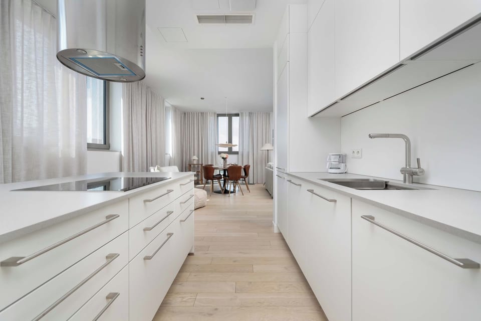 A bright, dual-sided kitchenette workspace features long white countertops, an induction cooktop, and modern fixtures. The generous layout offers plenty of room for culinary preparation.