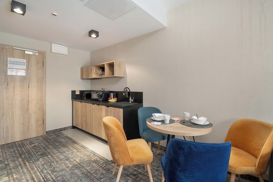 A cozy dining corner with two blue chairs and a small table arranged beside the kitchen. Soft lighting and warm wooden finishes create an intimate atmosphere.