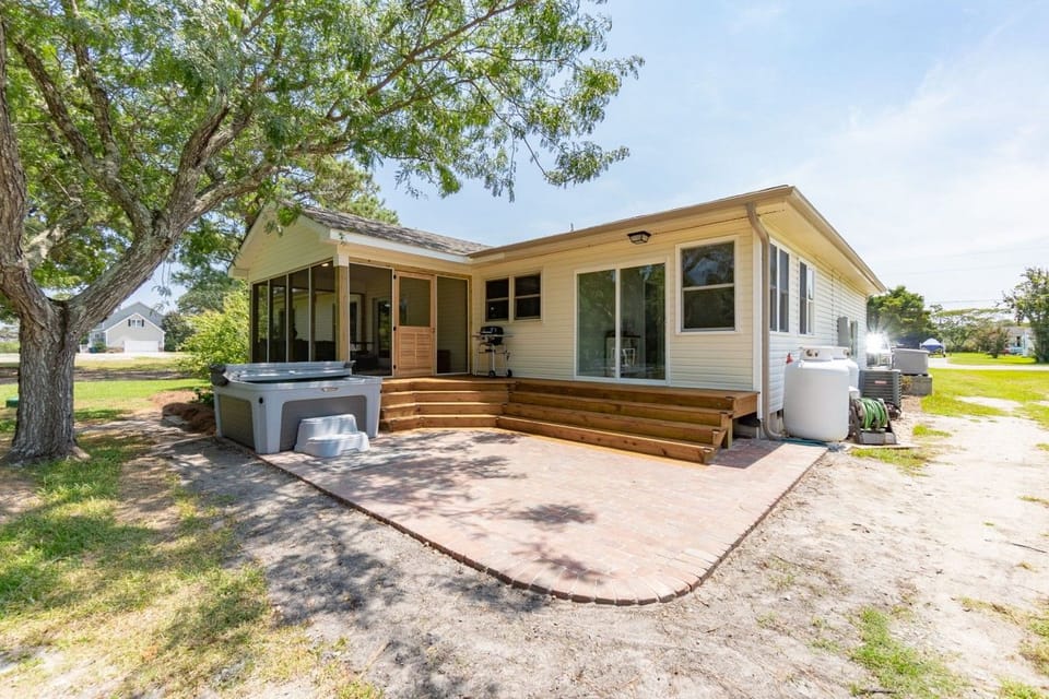 The whole backyard setup: screened porch, wide wooden steps, brick patio, hot tub, and room to roam.