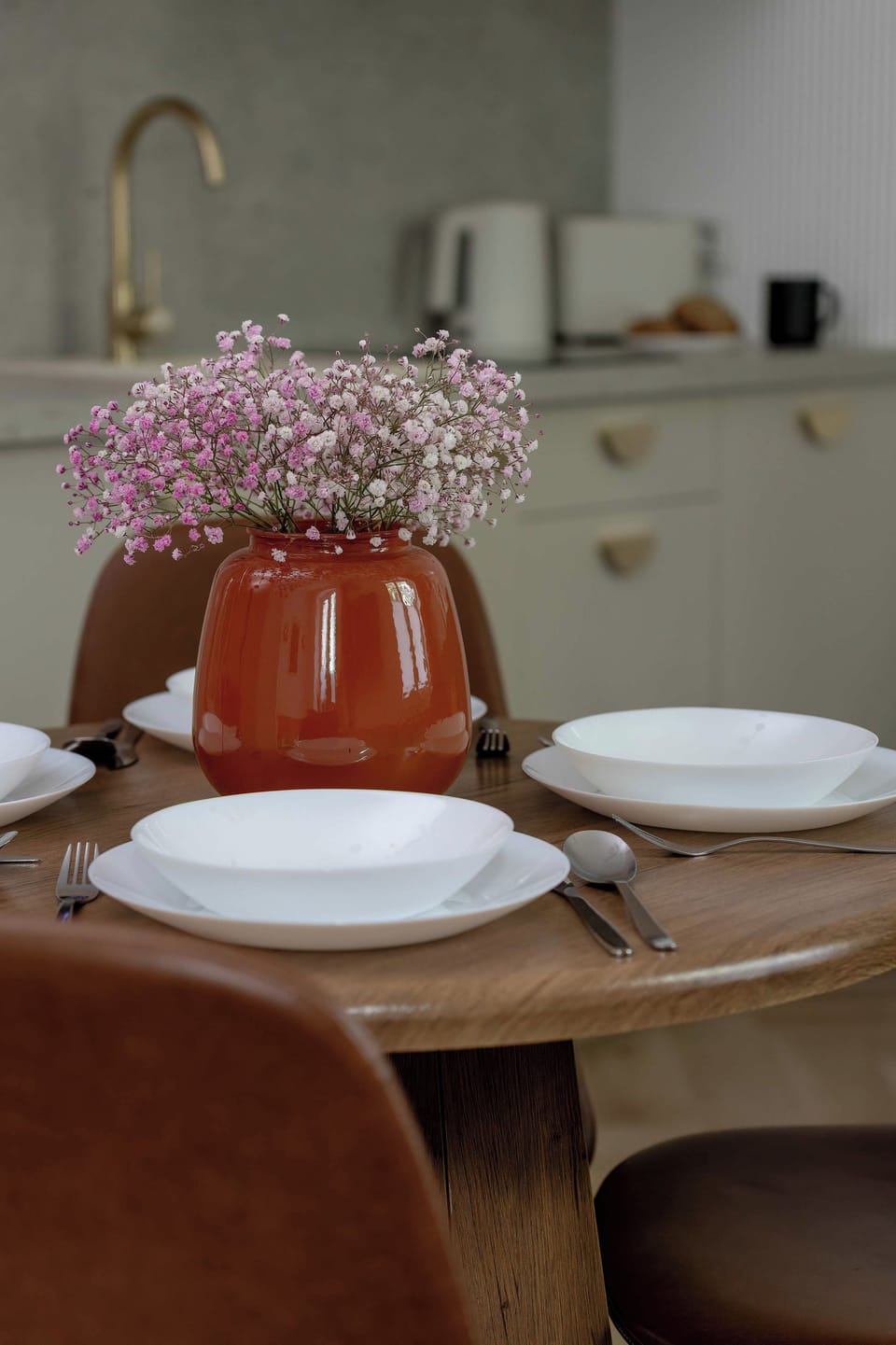 A close-up view highlights a decorated dining table with white plates and a vase of flowers. Warm wooden seating surrounds the cozy meal setting.