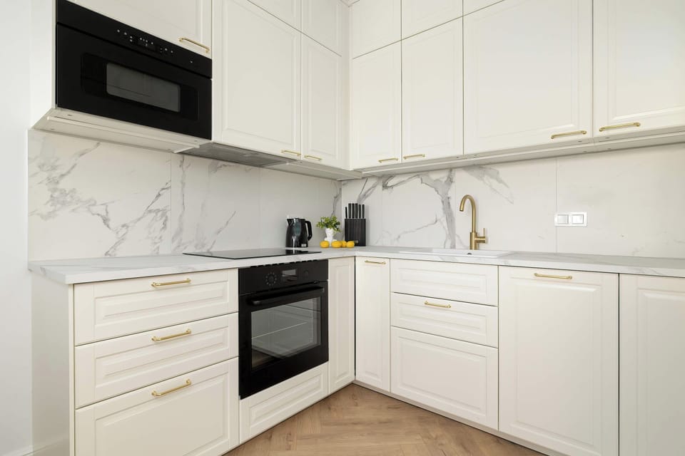 The modern kitchen boasts crisp white cabinetry and light-colored countertops. It is fully equipped with built-in appliances, including an oven and a dark microwave.