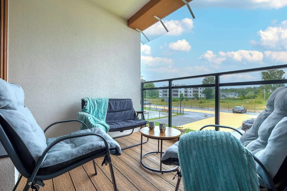 A sunny balcony offers a relaxing spot with outdoor chairs and a small glass-topped table. Light blue blankets are draped over the seating for added comfort.
