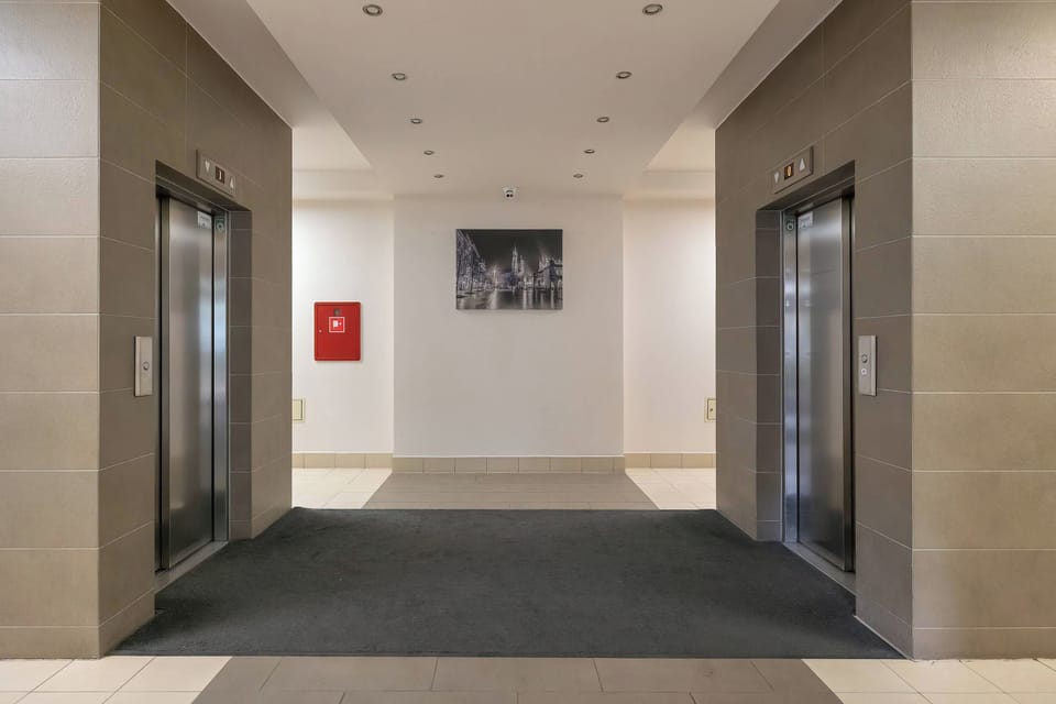 A modern residential building entrance hall with elevators, tiled walls, and a spacious communal area.