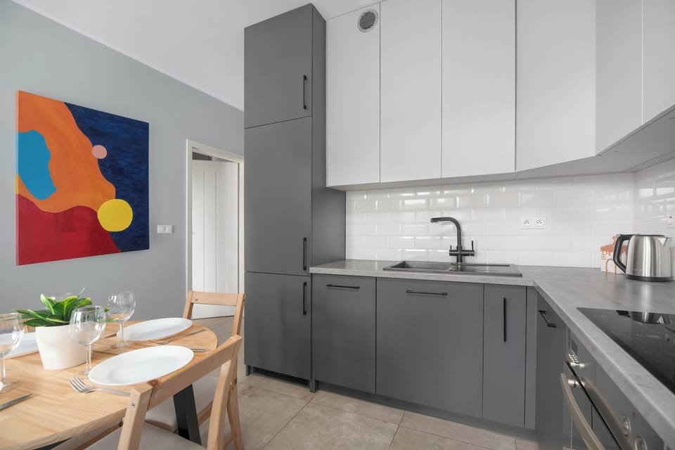 A modern kitchen with gray cabinets, white countertops, and a dining area with a wooden table and chairs.