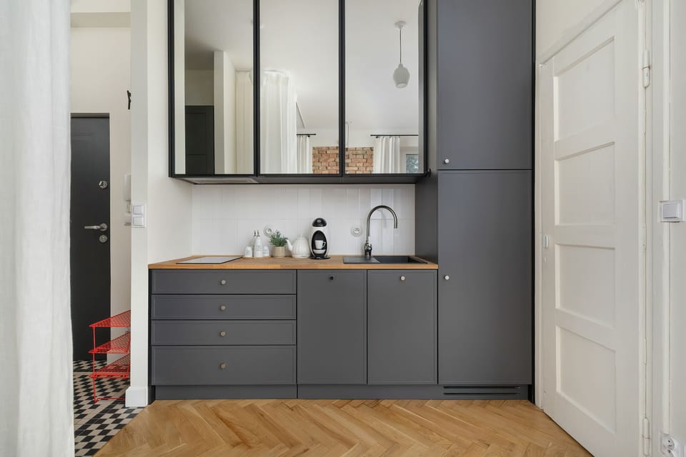 A bright kitchenette area with dark cabinets, a countertop, and a wooden floor.