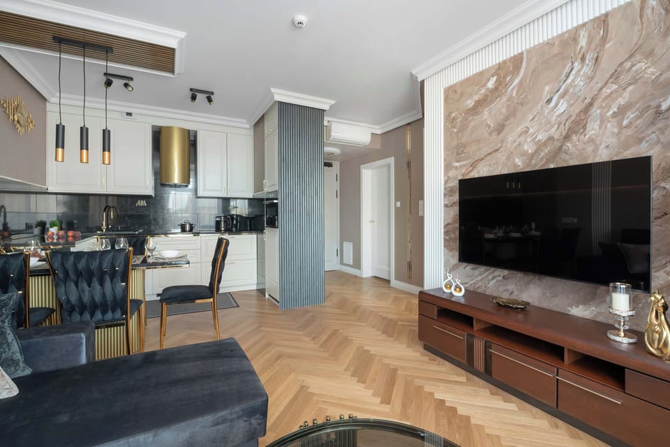 A cozy living room with a TV, gray sofa, and marble-effect wall.