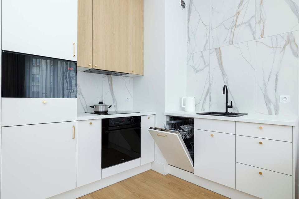 A modern kitchen with white cabinets, a built in oven and marble style backsplash. The well organized layout makes preparing meals convenient during your stay.