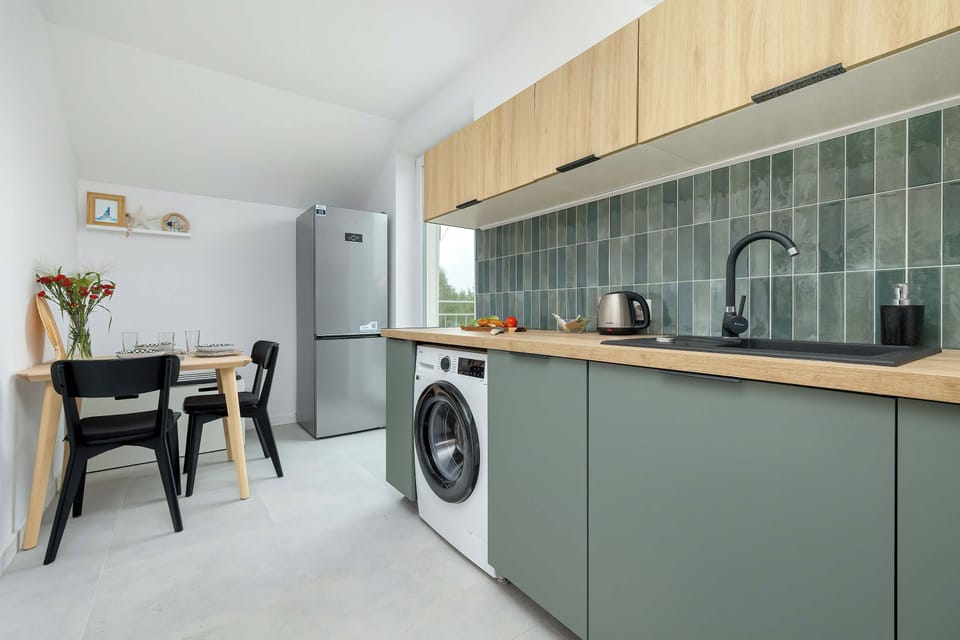 A closer view of the contemporary kitchen with green cabinetry, a washing machine, and a patterned backsplash.