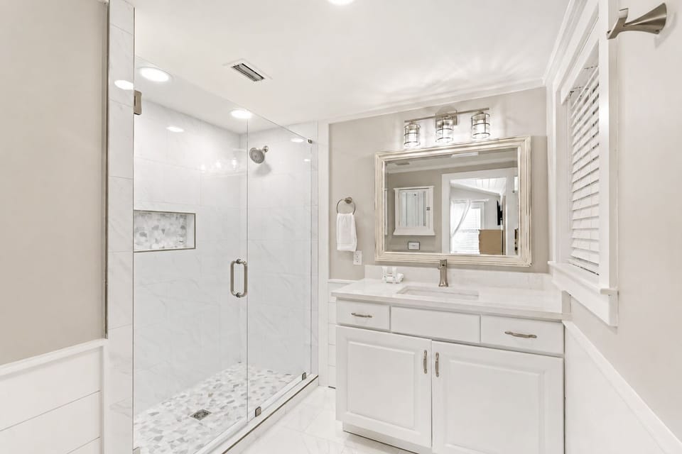 Updated bathroom with a large glass-enclosed walk-in shower, double vanity, and bright coastal finishes.