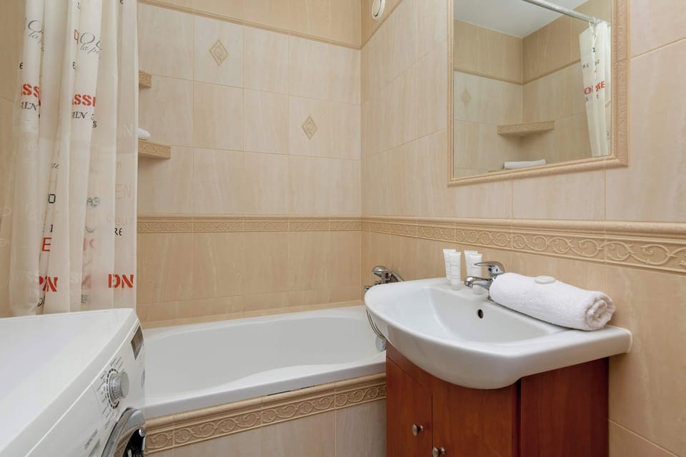 A compact bathroom with a sink, mirror, and light-colored tiled walls.