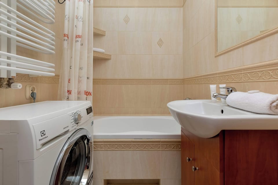 A bathroom featuring a washing machine, a bathtub, and light wood-effect wall panels.