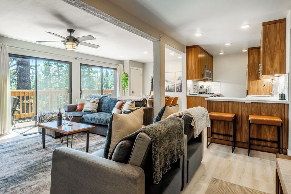 Unwind in your open-concept living space with a cozy seating area, modern kitchen, and deck overlooking the trees—perfect for relaxing after a day of adventure.