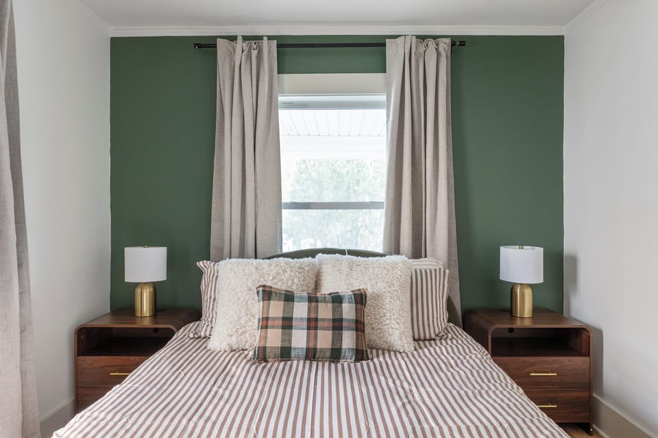 Main-level queen bedroom with a calming green accent wall, ceiling fan, and soft