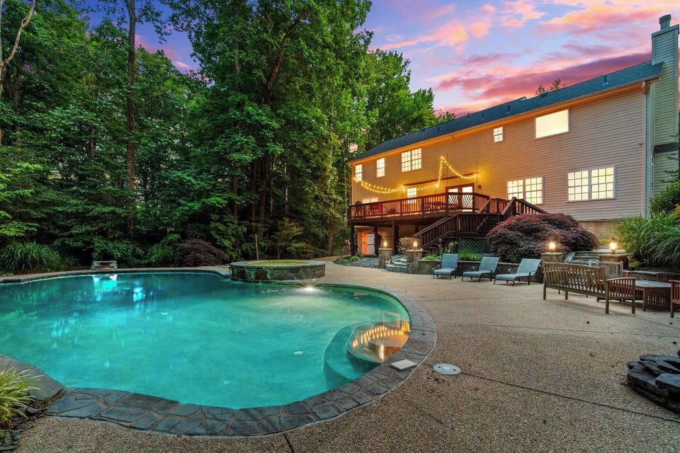 Private wooded backyard with pool, patio loungers, and a glowing deck