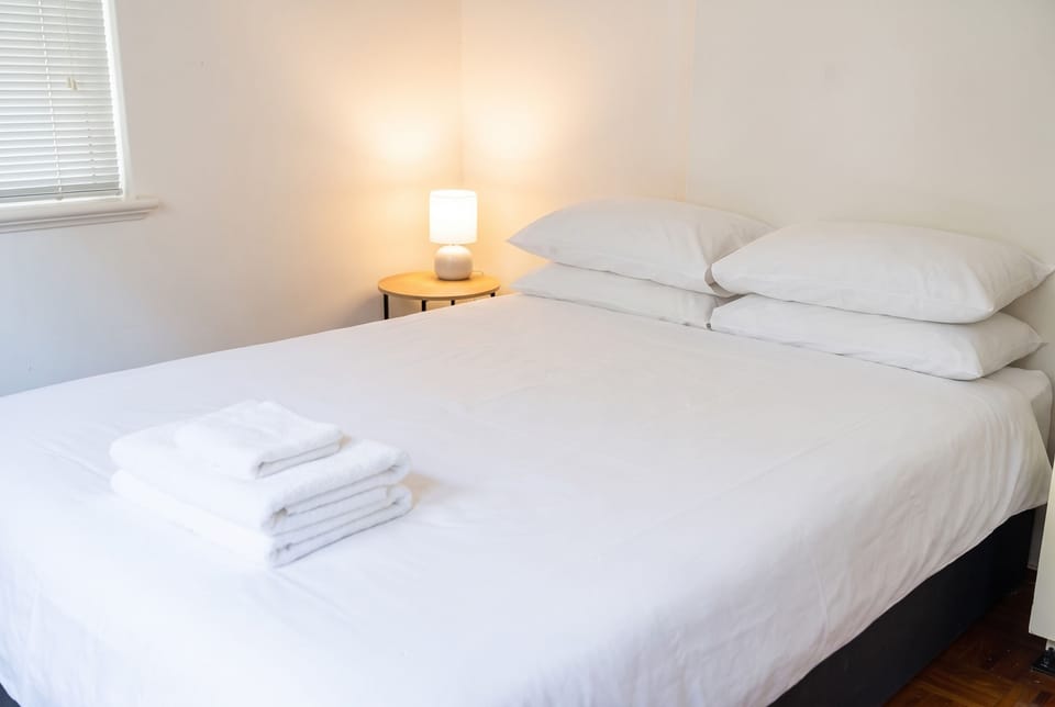 Queen bed with white linen, bedside lamp and fresh towels
