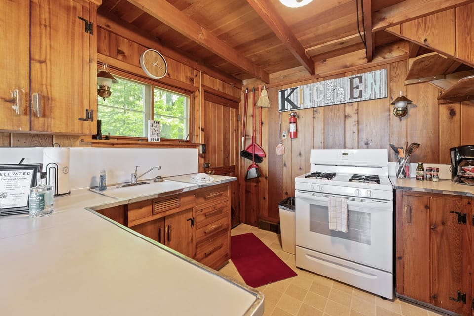 Relax in this cozy, wood-paneled bedroom with a ceiling fan, fresh linens, and large windows overlooking the peaceful wooded surroundings.
