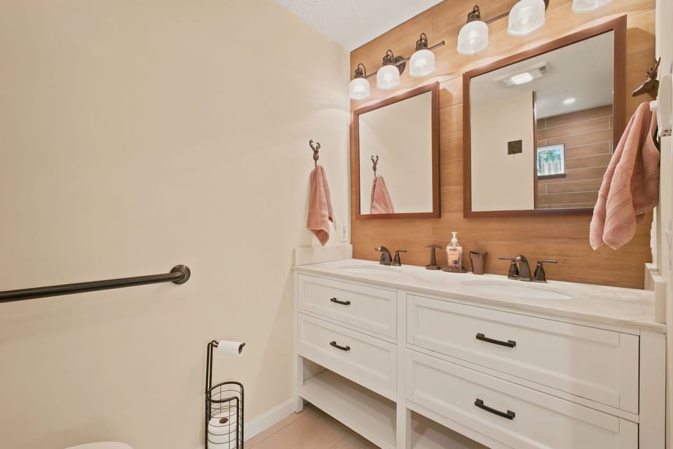 A bright bathroom with a double vanity and a wood-look accent wall.