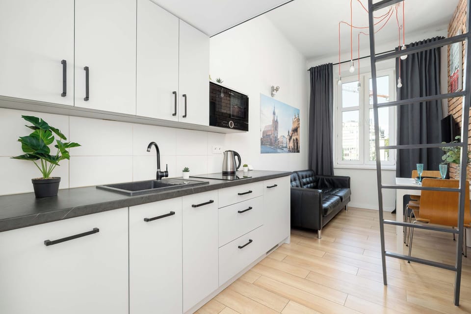 A modern kitchenette with white cabinets, a dark countertop, and a sink. The open layout connects the kitchen with the studio's living area.