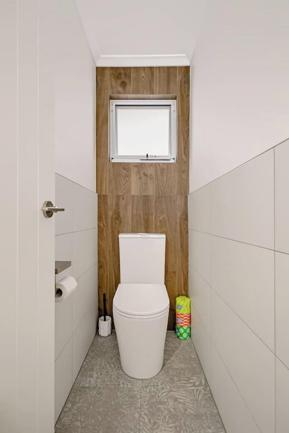 Separate private toilet with timber-look feature wall, natural light from the window, and floral-pattern floor tiles.