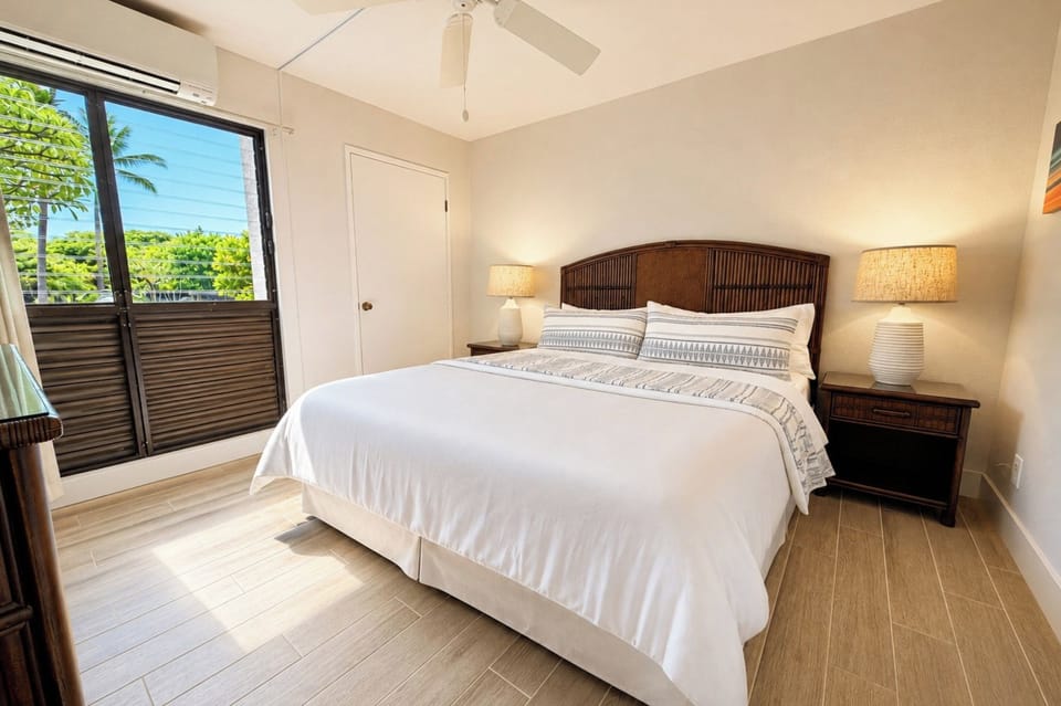 Primary bedroom at Napili Point B31 — king bed, private lanai access, and lush tropical views through the sliding glass door NAP-B31