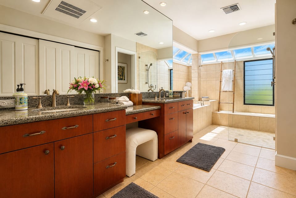 A vanity stool sits between the dual sinks in the ensuite bathroom, with the soaking tub and glass shower just beyond. KBV-16B3