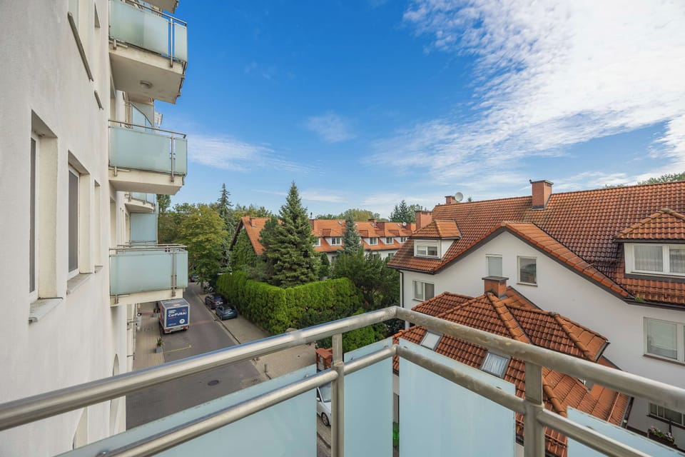 A bright, open balcony overlooking a charming residential neighborhood filled with classic red-tiled roofs. Clear blue skies make this a highly inviting spot for outdoor relaxation and fresh air.