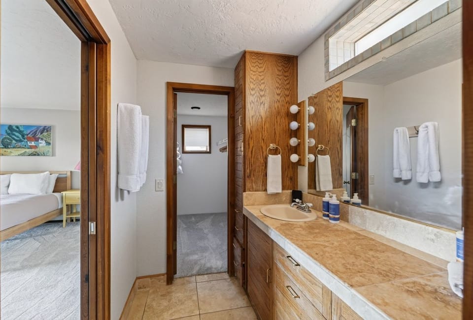 Step into your private bathroom with warm wood accents and fresh towels ready for you. The vanity offers plenty of space to spread out, and soft lighting above the mirror creates a welcoming glow.