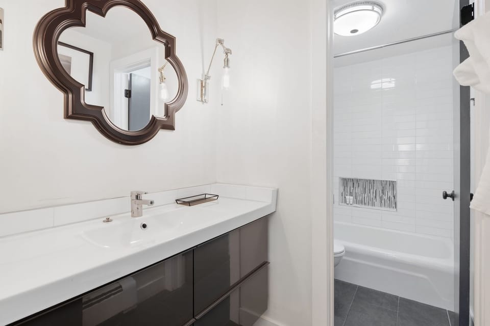 A modern bathroom vanity with glossy drawers and an adjoining tub and shower area.