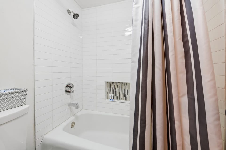 A white tiled shower and tub combo with a recessed niche and striped curtain.