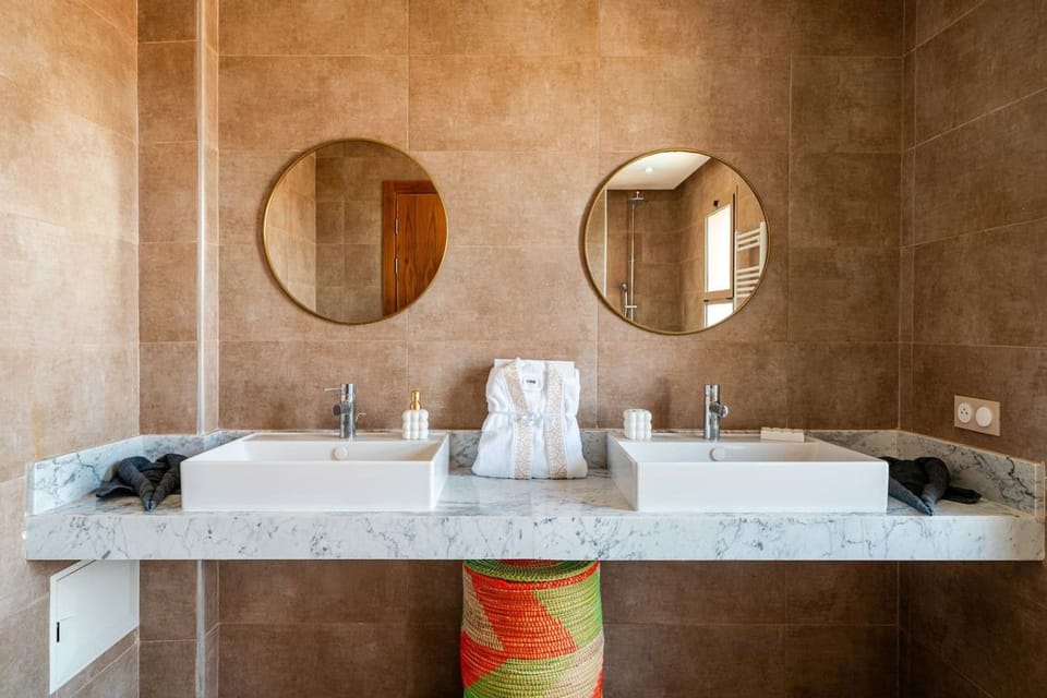Twin bathroom basins with chrome taps and round mirrors provide a generous vanity area at the villa.