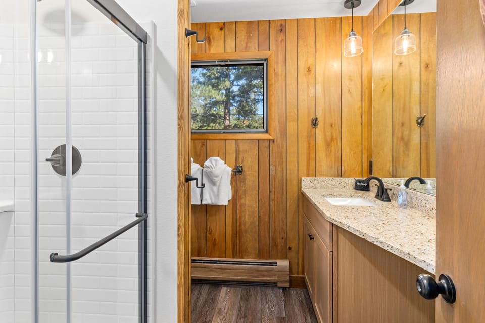 Glass-enclosed shower with white subway tile sits beside wood-paneled walls and a granite vanity countertop.