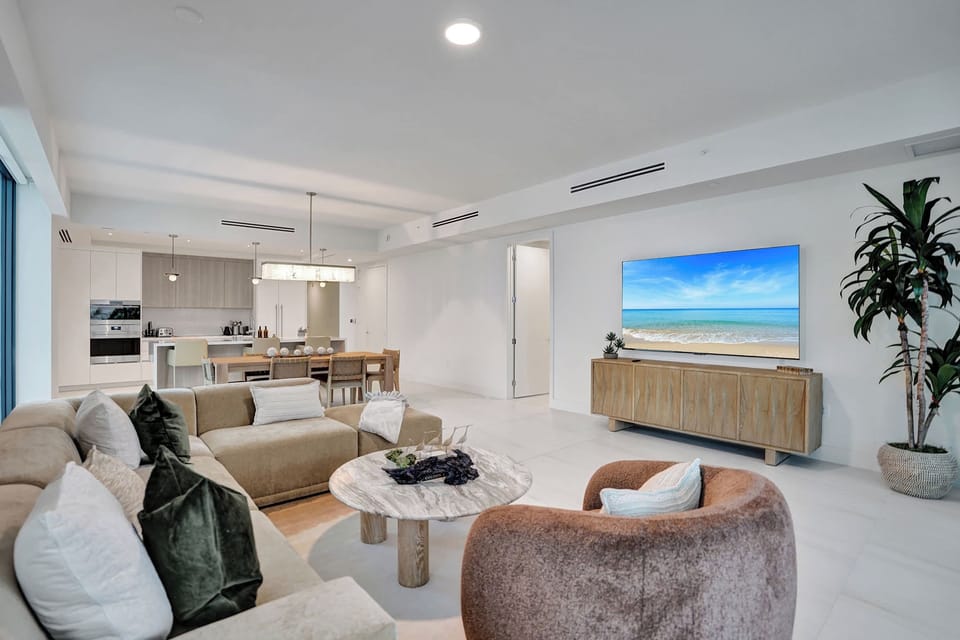 Bright living area with curved sectional, round marble coffee table, and ocean-art TV wall.