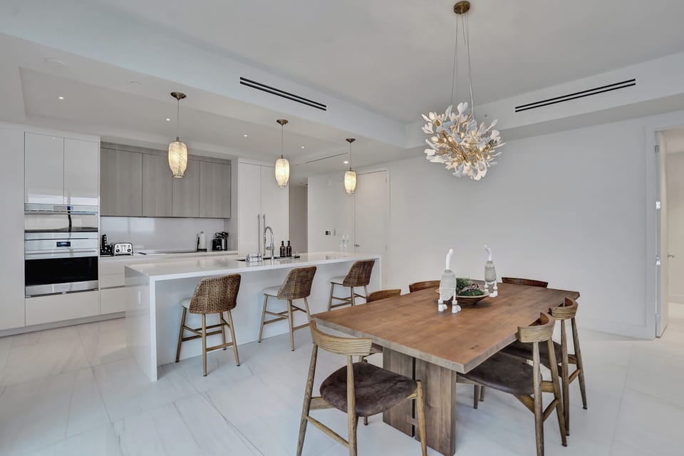 Open dining room with wood table and sculptural chandelier, kitchen island and pendant lights in the background.