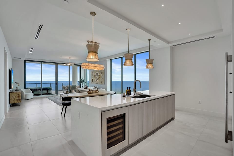 Open kitchen with a waterfall island, wine fridge, and direct ocean views through floor-to-ceiling glass.