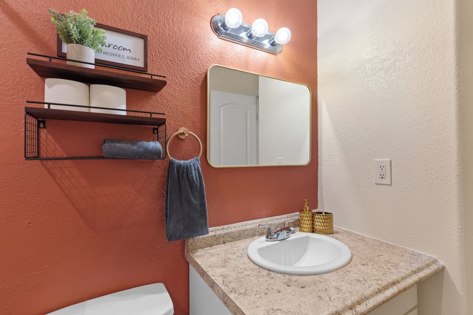 Step into your own private sanctuary with this thoughtfully designed bathroom. The warm coral accent wall creates an inviting atmosphere while open shelving keeps fresh towels and essentials within easy reach.