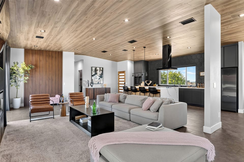 Open-concept great room with sleek lounge seating, a statement kitchen, and warm wood ceiling details.