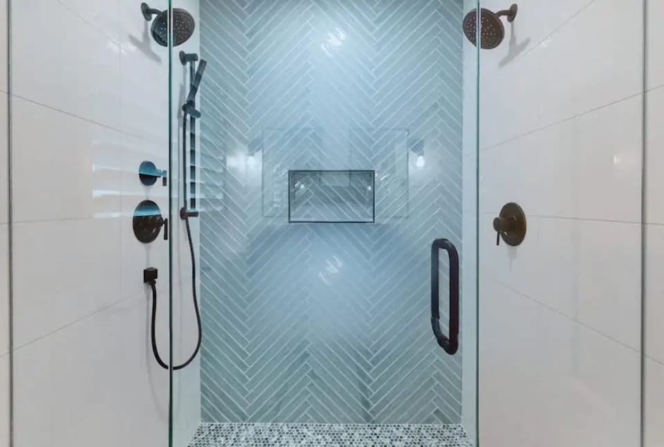 Walk-in shower featuring a herringbone tile accent wall and dual shower fixtures.