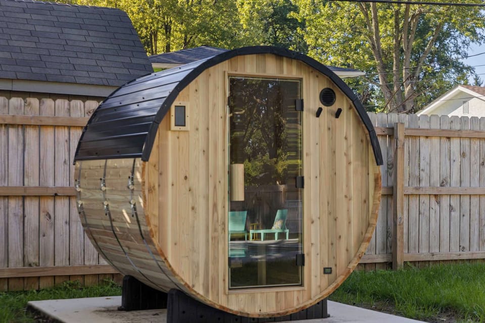 Outdoor barrel sauna with glass door set in a private backyard.