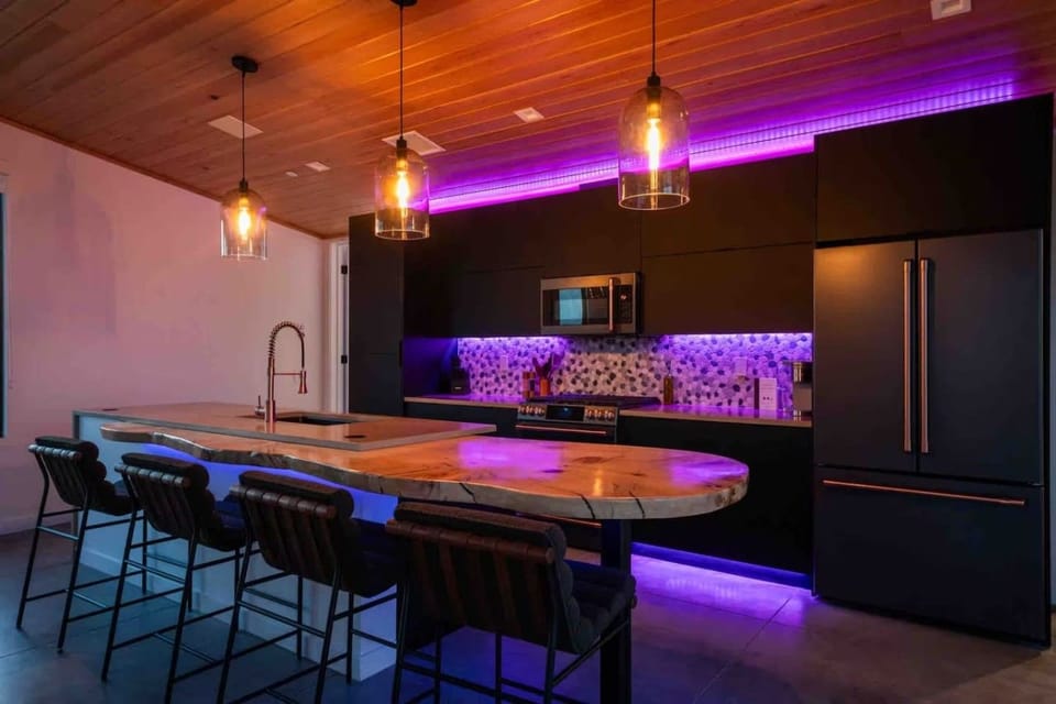 A sleek, fully equipped kitchen with spacious island seating and colorful ambient lighting.